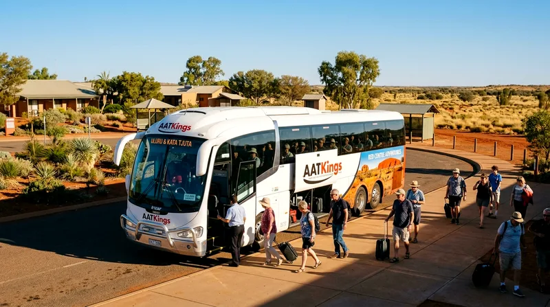 Group tour coach with passengers in Yulara resort precinct with resort buildings visible.