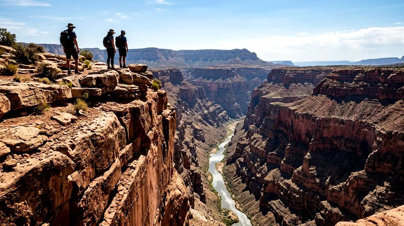 Three hikers on canyon rim looking down into deep red gorge with river bed visible.