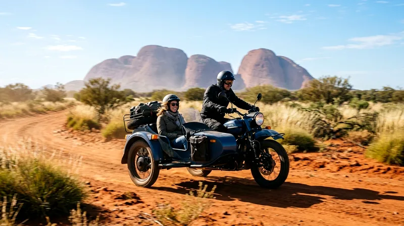 Motorcycle with sidecar carrying passenger riding across red desert landscape.