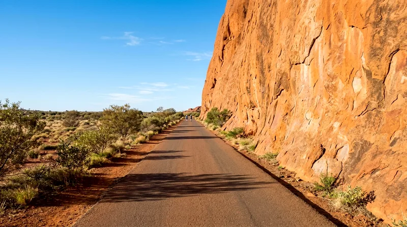 Sealed walking trail with Uluru cliff wall rising directly on the side.