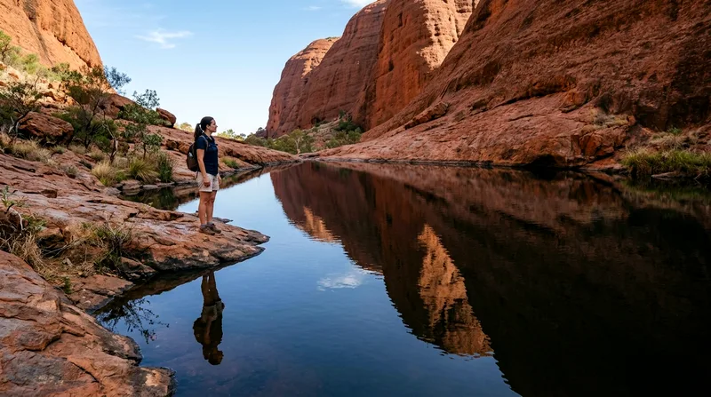 Visitor at Mutitjulu Waterhole with reflected rock formations in dark still water.