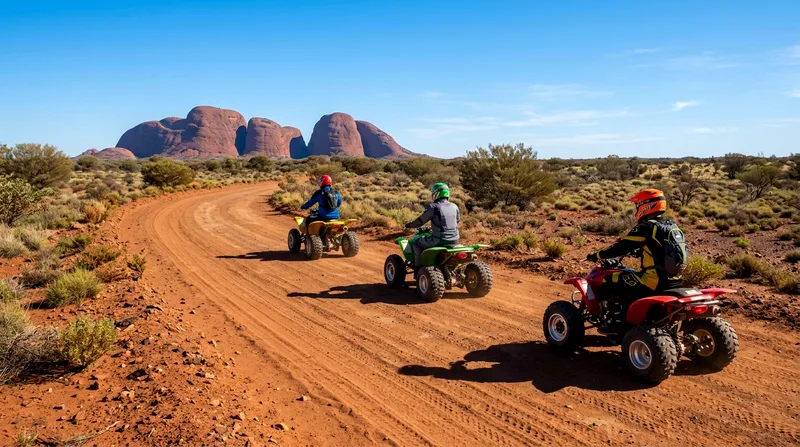 Three quad bike riders in single file on marked dirt track with Kata Tjuta rocks visible.
